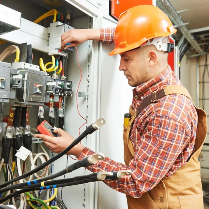 Electrician in a hard hat testing wiring inside a commercial electrical panel
