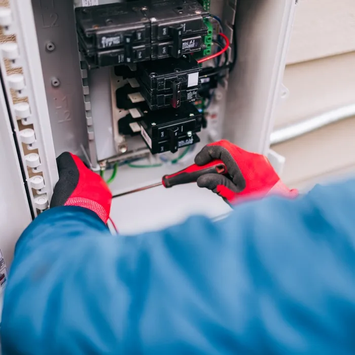Electrician wearing red gloves working inside a residential electrical panel